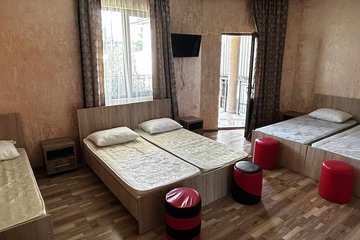 A room with a large bed, two smaller beds, a TV, and a view of the outside.