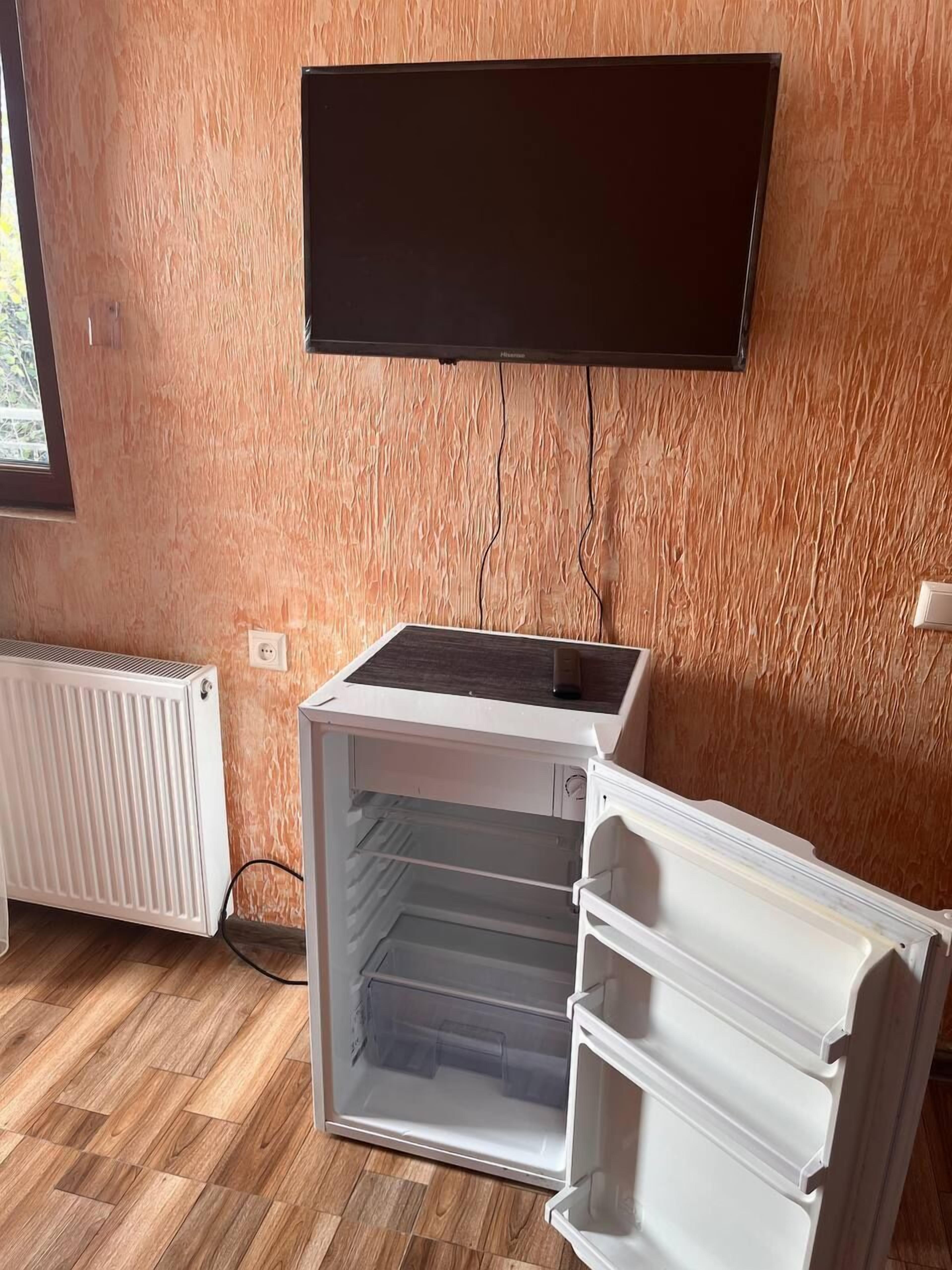 Una habitación con un radiador blanco, un refrigerador blanco y un televisor de pantalla plana montado en la pared.