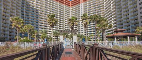 A high-rise hotel with multiple balconies, palm trees, and a gated entrance.