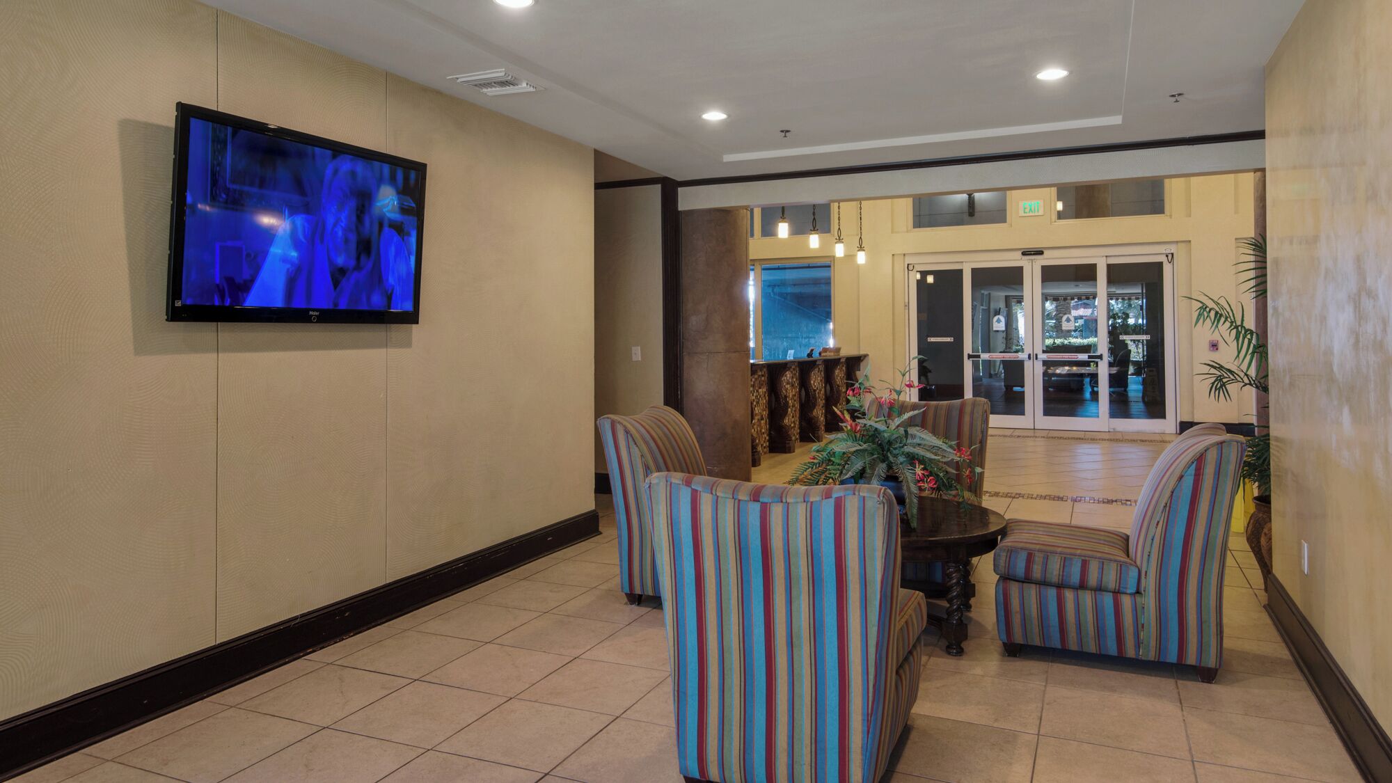 A lobby with striped armchairs, a television mounted on the wall, and a reception desk with a glass door leading outside.