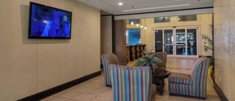 A lobby with striped armchairs, a television mounted on the wall, and a reception desk with a glass door leading outside.