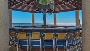 A bar area with a view of the ocean, featuring a wooden bar counter and wicker chairs. - Amazing Gulf Views! Spa, Pool, Tiki Bar and More! (Panama City Beach)