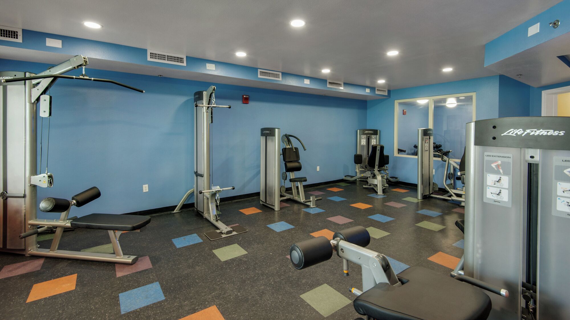 A gym with various exercise machines, a mirror, and a patterned floor.