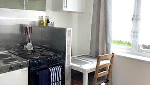 Kompakti keittiö, jossa on liesi, uuni ja ruokapöytä sekä yksi tuoli.