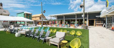 An outdoor seating area with rows of chairs and tables, a building with a storefront, and a grassy lawn.
