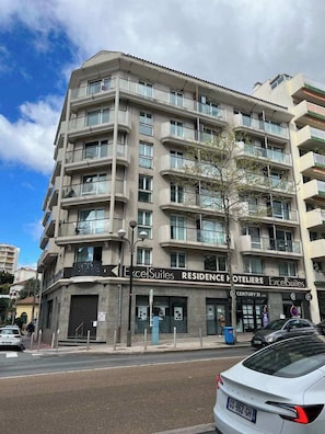 A multi-story hotel with balconies, a sign for 'Excelsuites Residence Hotelier,' and a visible entrance.