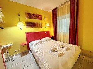 A hotel room with a bed, two wall-mounted lamps, a painting, and a window with curtains.