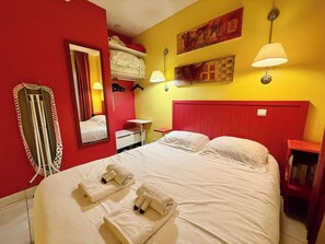 A hotel room with a bed, a mirror, a red wall, and a yellow wall with artwork.