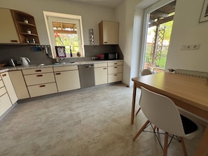 Ett kök med matplats, utrustat med skåp, en diskho, en mikrovågsugn och ett fönster med utsikt över grönområden.