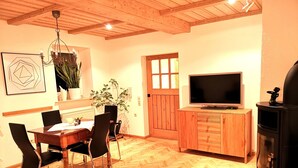 A wooden interior with a dining table, chairs, a TV, and a fireplace. - The Property (Rentweinsdorf)