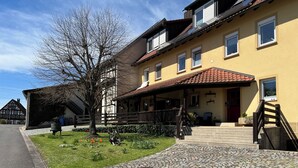 A traditional building with a cobblestone entrance, a covered porch, and a staircase leading to the entrance. - The Property (Rentweinsdorf)