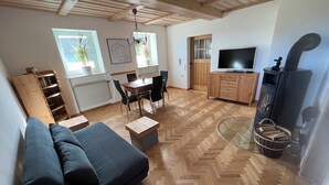 A cozy living room with a sofa, a red chair, a dining table with chairs, a TV, a fireplace, and a bookshelf. - The Property (Rentweinsdorf)