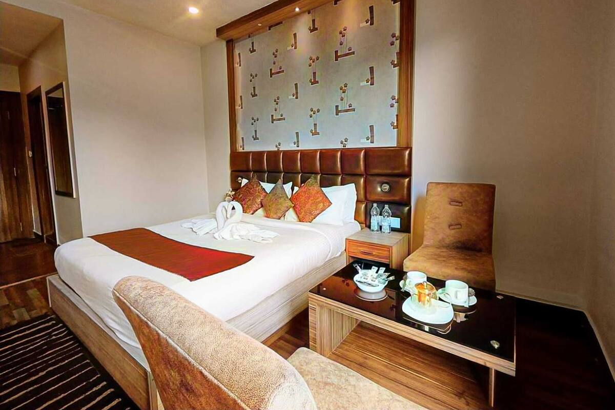A hotel room with a large bed, a wooden headboard, a bedside table with a lamp, and a chair.