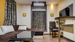 A modern living room with a sectional sofa, a glass coffee table, a leather armchair, and a flat-screen TV mounted on the wall. - Kings Resort (Gobindpur)