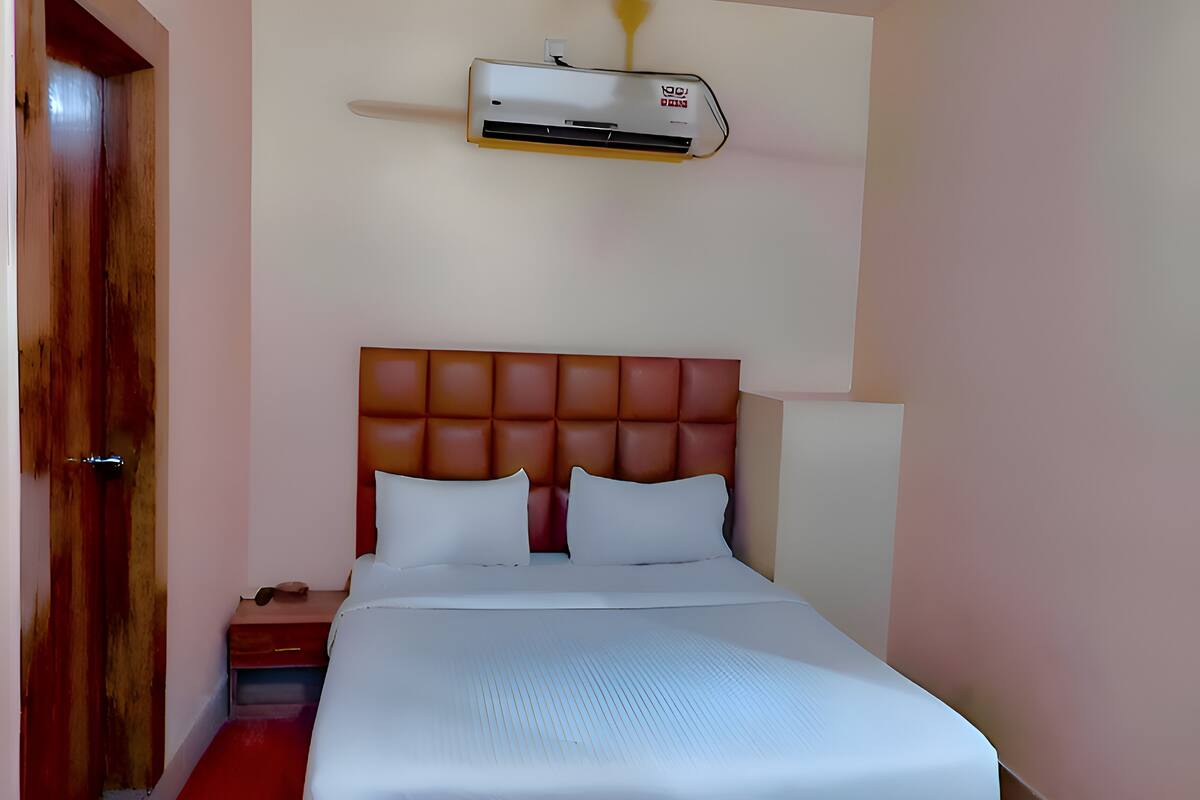 A bedroom with a bed, a wooden door, a nightstand, and an air conditioning unit on the wall.