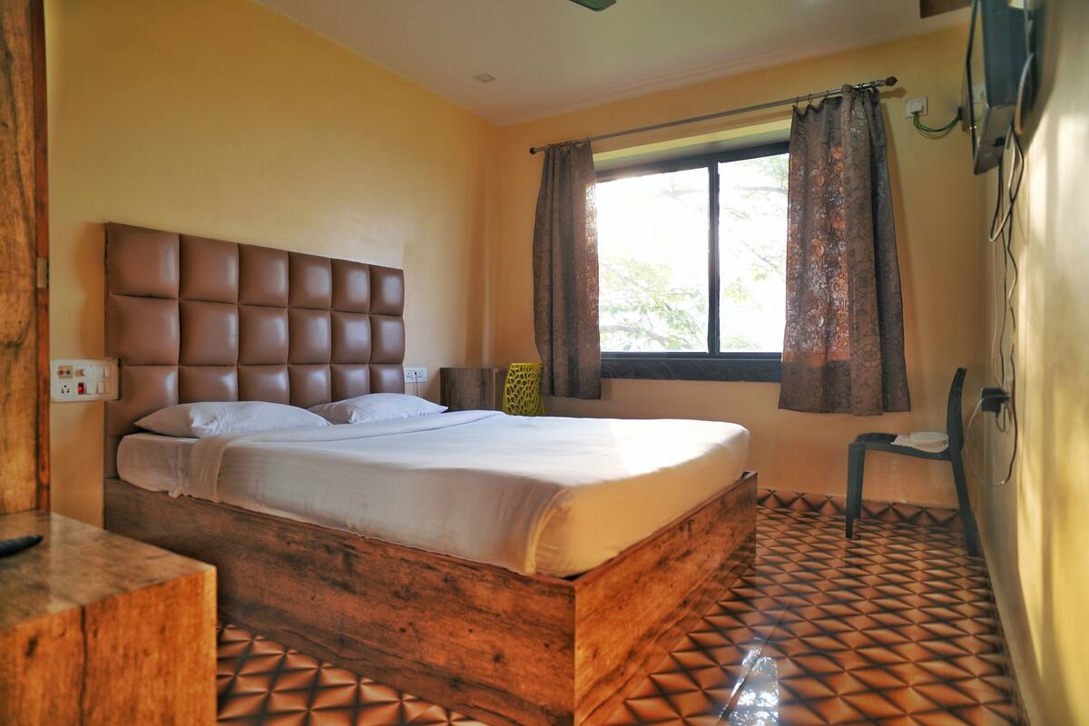 A bedroom with a wooden headboard, a bed with white linens, a window with curtains, and a patterned floor.