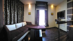 A modern living room with a dark brown sofa, a coffee table, and a flat-screen TV mounted on the wall. - Kings Resort (Gobindpur)