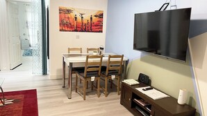 A dining area with a table and chairs, a flat-screen TV mounted on the wall, and a painting above the table. - Crescent Apartment - Two bedroom (Romford)