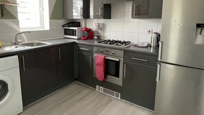 A modern kitchen with dark cabinets, a stainless steel refrigerator, a microwave, a red coffee machine, and a gas stove. - Crescent Apartment - Two bedroom (Romford)