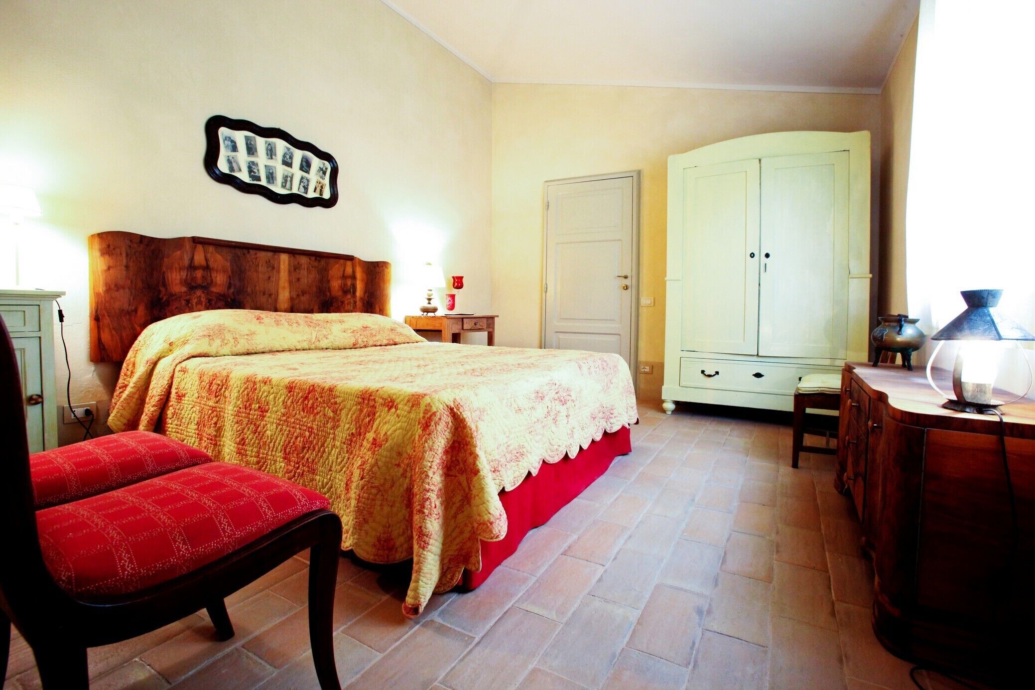 A bedroom with a bed, a chair, a wardrobe, and a desk with a lamp.