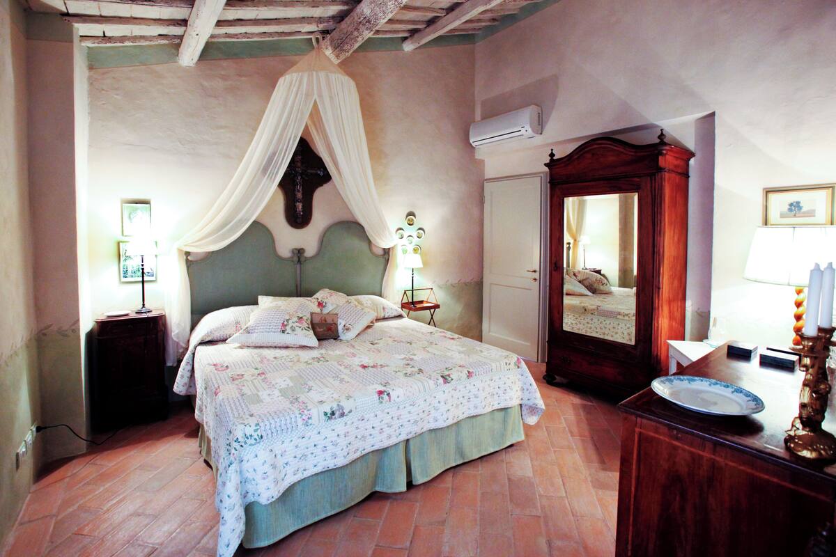Un dormitorio con cama con dosel, un armario de madera, una mesita de noche con lámpara y un espejo.