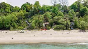 Una playa con escaleras de madera que conducen a una zona boscosa, agua turquesa cristalina y una playa de arena.