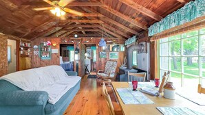 Interior acogedor de una cabaña con techo de madera, un sofá, una mesa de comedor y un ventanal con vistas al exterior.