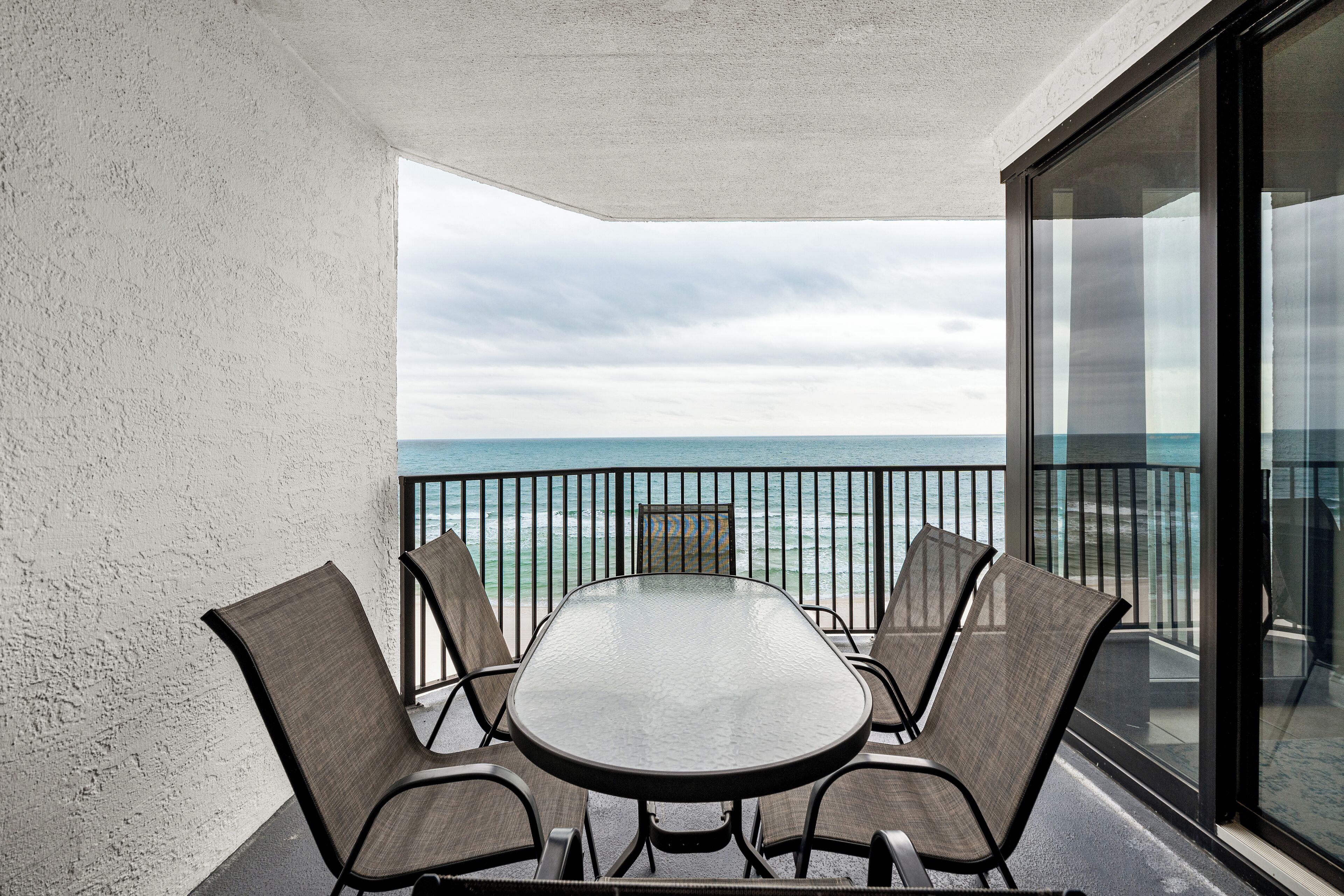 A balcony with a table and chairs, overlooking the ocean.