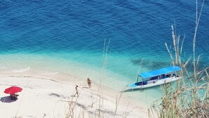 Una playa con agua turquesa cristalina, un bote y un paraguas rojo en la arena.