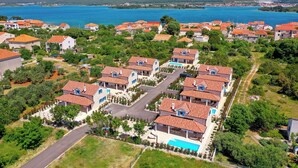 Un quartier résidentiel où les maisons sont coiffées de toits en tuiles rouges, entourées de verdure, et où l’on aperçoit une grande étendue d’eau au loin.