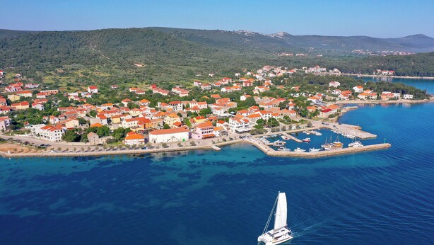 Vue aérienne d’une ville côtière avec des maisons, un port de plaisance et un voilier.