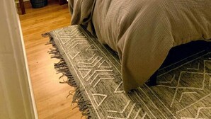 Un lit bien fait, avec une tête de lit, deux lampes de chevet, un tapis à motifs et une fenêtre avec des stores.