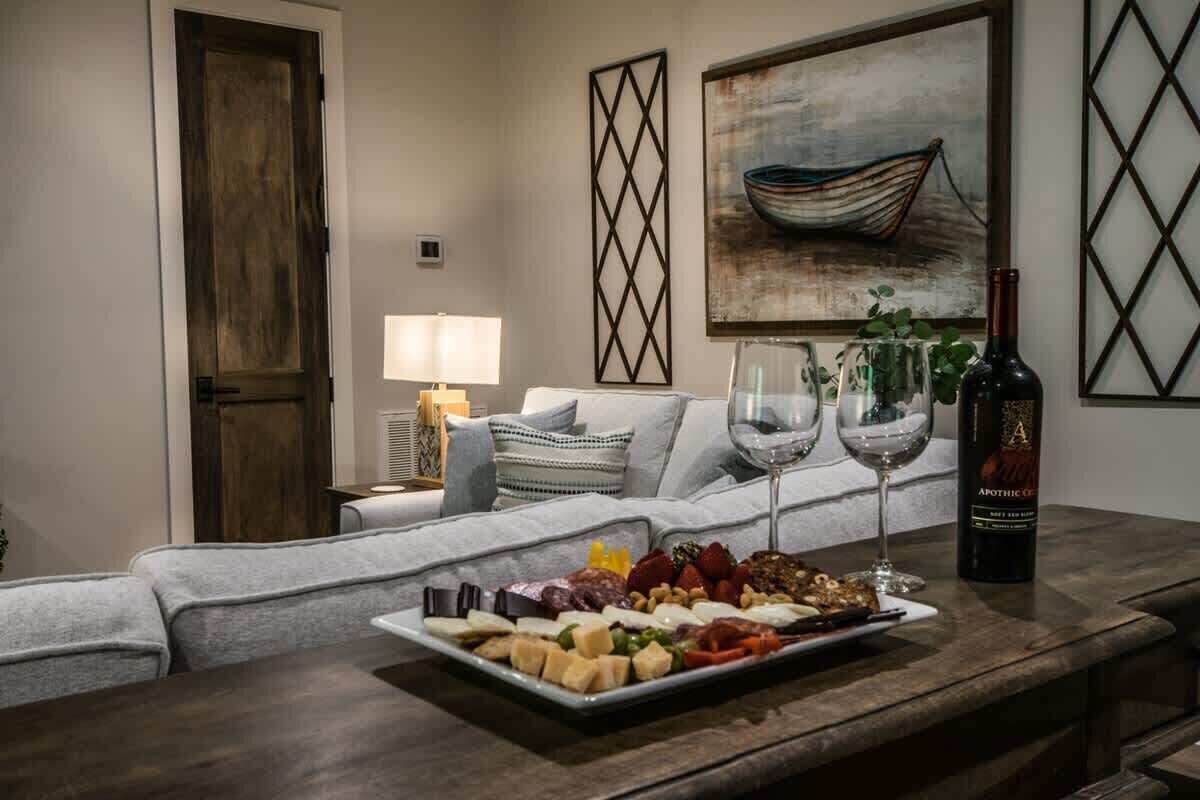 Een gezellige woonkamer met een houten salontafel waarop een charcuterieplank en wijnglazen staan, een bank met gekleurde kussens, en een schilderij van een boot aan de muur.