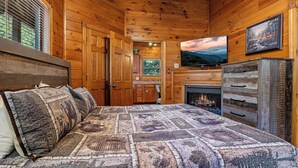 L’intérieur d’un chalet en bois, avec un lit, une cheminée, un téléviseur et un tableau accroché au mur.