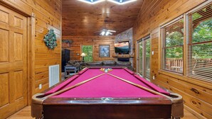 Une table de billard recouverte d’un feutre rouge, avec des parois en bois et un ventilateur de plafond.