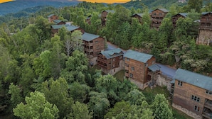 A resort with multiple wooden cabins surrounded by dense forest, featuring balconies and a mountainous backdrop. - Views, Hot Tub, Fireplace, Resort Pool, + Game Room (Gatlinburg)