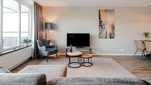 Una sala de estar moderna con un amplio ventanal, un sillón gris, una mesa de centro redonda y un televisor de pantalla plana.