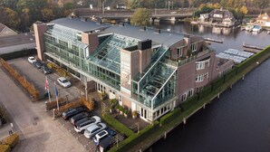 Un hotel moderno con fachada de vidrio, estacionamiento y vista al río.