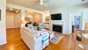 A living room with a white sofa, patterned armchairs, a fireplace, and a ceiling fan.
