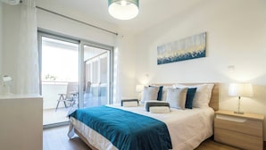 A bedroom with a bed, bedside tables, a desk, and a sliding glass door leading to a balcony. - Coastal Haven apartment Lagos (Lagos)
