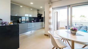 A modern kitchen with grey cabinets, a black countertop, and a dining area with a round table and chairs. - Coastal Haven apartment Lagos (Lagos)