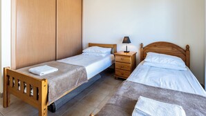 A bedroom with two single beds, a wooden wardrobe, a bedside table with a lamp, and a small drawer unit. - Apartment Lesley - great location! (Armação de Pêra)