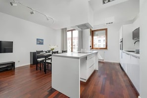Una cocina moderna con una isla central, un comedor con sillas, un televisor de pantalla plana y una ventana con cortinas.