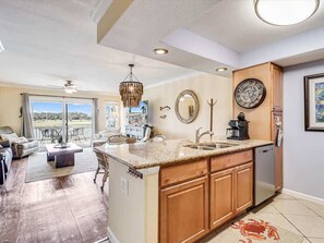 A spacious living area with a large window, a dining area, and a kitchen with wooden cabinets and a granite countertop.