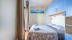 A bedroom with a bed, a painting of sailboats, and blue cabinets. - Elegante Appartamento con Spiaggia sul Mare di Bari (Bari)