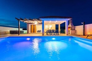 En swimmingpool med et overdækket opholdsområde og en terrasse.