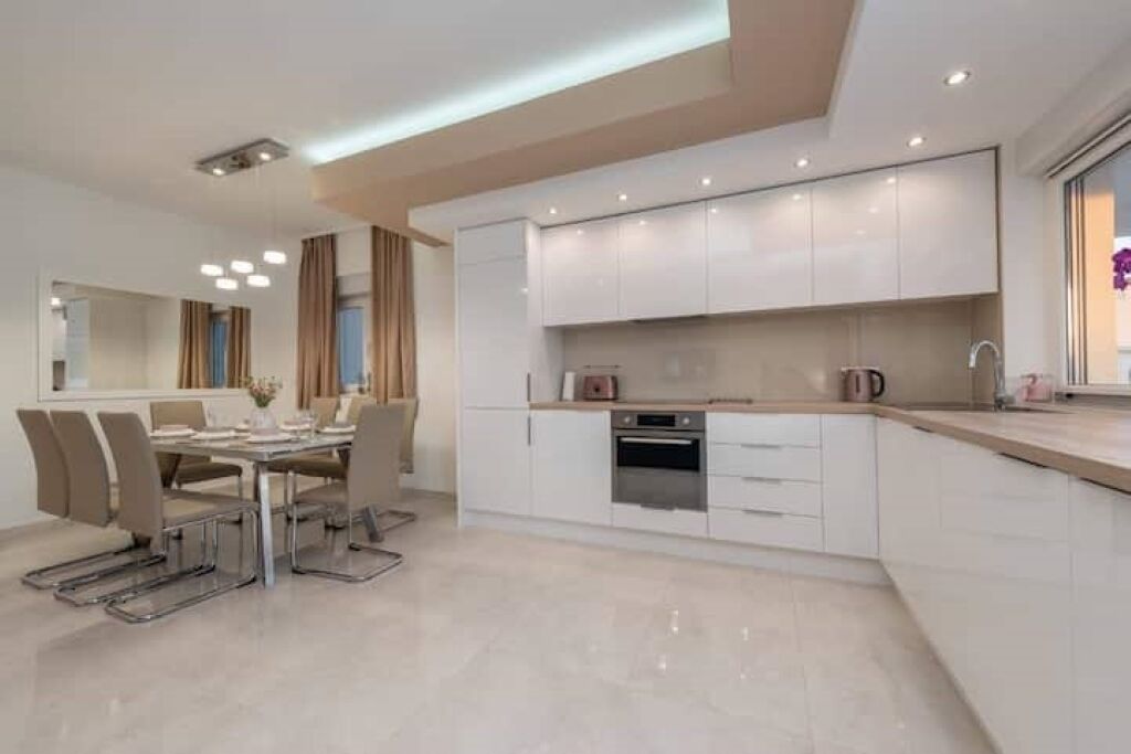 Une cuisine moderne avec des meubles blancs, un four encastré et un coin repas comprenant une table et des chaises.