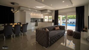 Una sala de estar moderna con un sofá gris, comedor con sillas y una cocina al fondo.