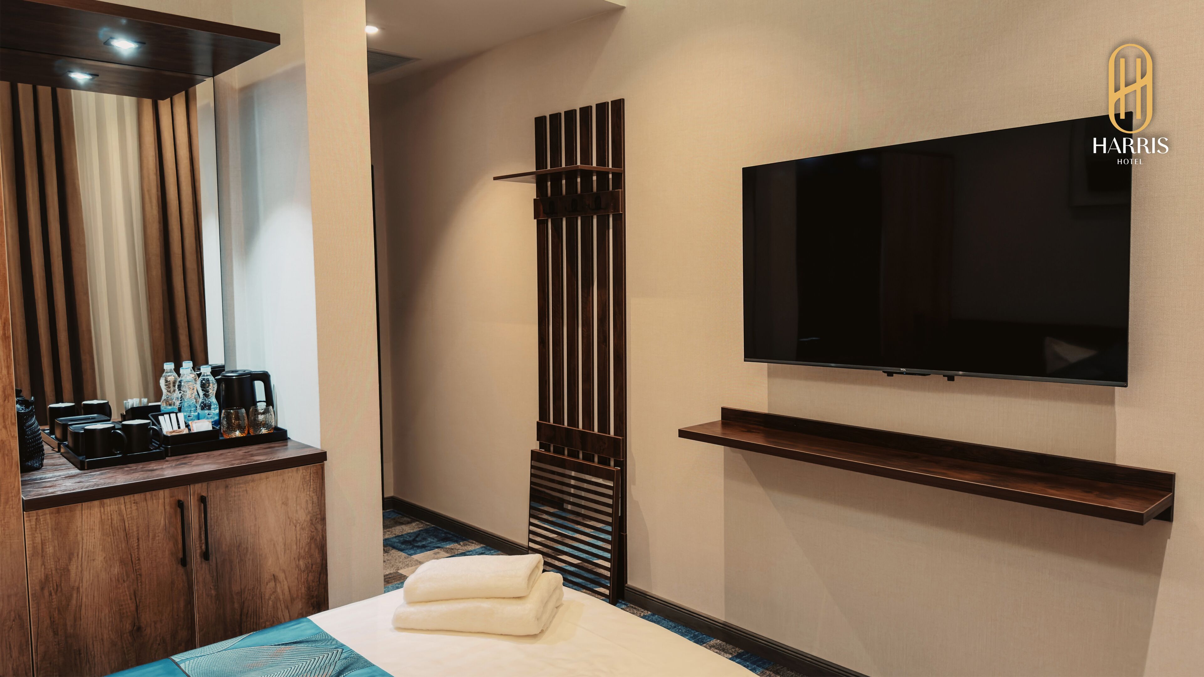 A hotel room with a bed, a TV mounted on the wall, a wooden cabinet, and a bedside table with toiletries.