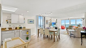 A modern kitchen with white cabinets, a dining area with a table and chairs, and a living room with a sofa and a view of the ocean. - ~ Beach Breeze ~   Beautiful Oceanfront 3 Bed/2 Bath Condo (Myrtle Beach)